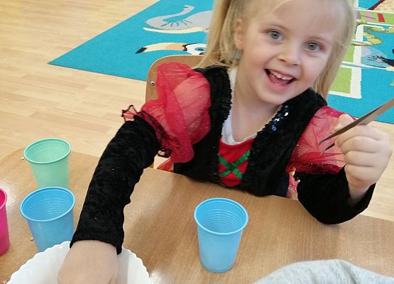 Dziewczynka  za pomocą pęsety przenosi groszki z miski do kubka