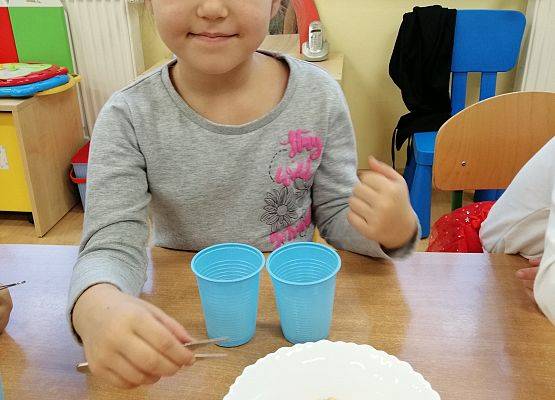 Dziewczynka  za pomocą pęsety przenosi groszki z miski do kubka