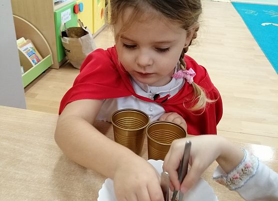 Dziewczynka  za pomocą pęsety przenosi groszki z miski do kubka