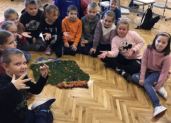 Uczniowie siedzą na podłodze prze makiecie Polski