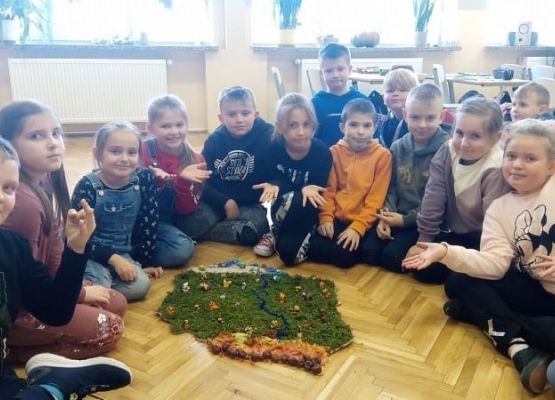 Uczniowie siedzą na podłodze prze makiecie Polski