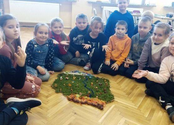 Uczniowie siedzą na podłodze prze makiecie Polski