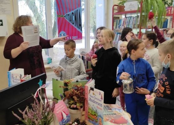 Uczniowie stoją w bibliotece i słuchają informacji od nauczyciela