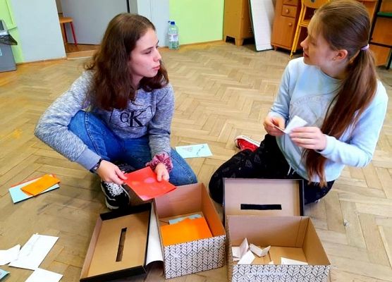 Uczennice siedzą na podłodze i segregują kartki z okazji Dnia Życzliwości i Pozdrowień