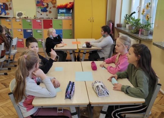 Uczniowie siedzą przy stolikach i pracując w grupach