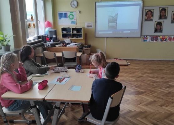 Uczniowie siedzą w ławkach i oglądają prezentację.