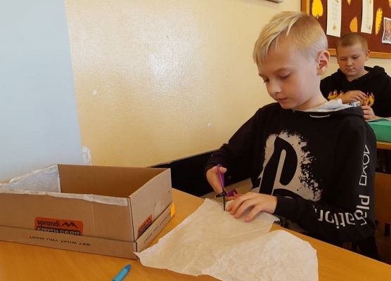 Uczeń obcina nożyczkami papier