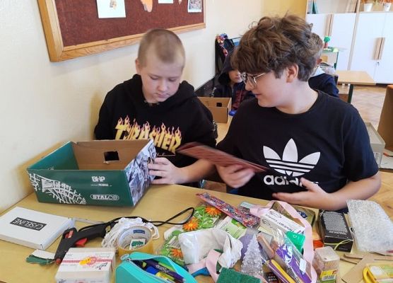 Dwaj uczniowie siedzą w ławce i wycinają elementy pokoju