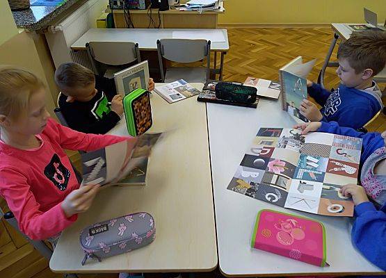 Uczniowie siedzą przy stoliku i oglądają książki