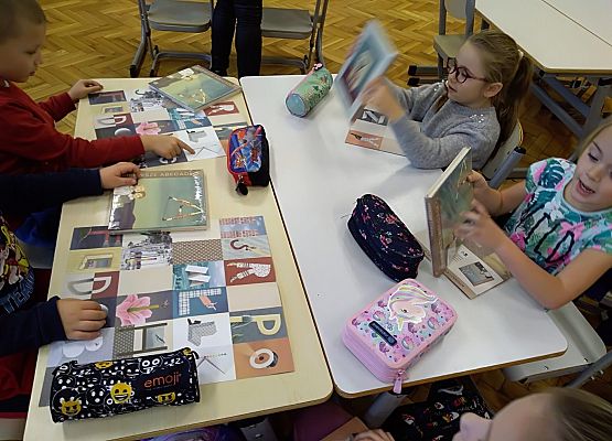 Uczniowie siedzą przy stoliku i oglądają książki