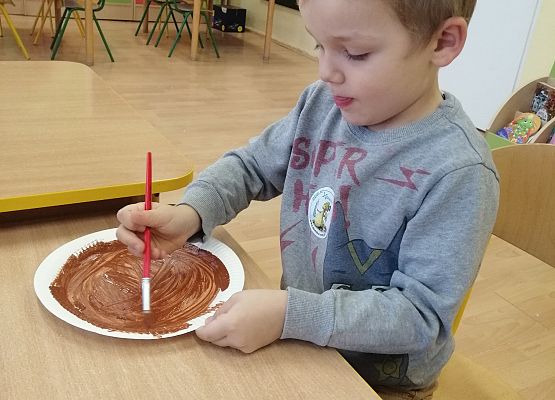 Chłopiec maluje farbą papierowy talerz