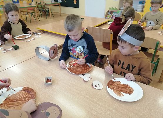 dzieci malują papierowe talerze brązową farbą