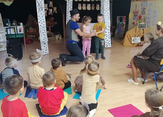 Przedszkolaki siedzą na podłodze i oglądają sztuczki magika