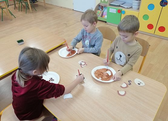 dzieci malują papierowe talerze brązową farbą