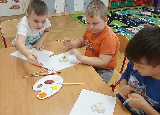 Chłopcy siedzą przy stoliku i malują farbami