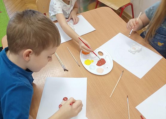 Dzieci siedzą przy stoliku i malują misie