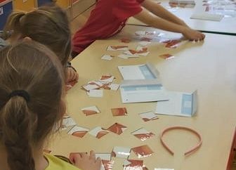 Dzieci siedzą przy stolikach i układają puzzle