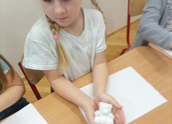 Dziewczynka siedzi przy stoliku i trzyma w dłoniach gipsowego misia