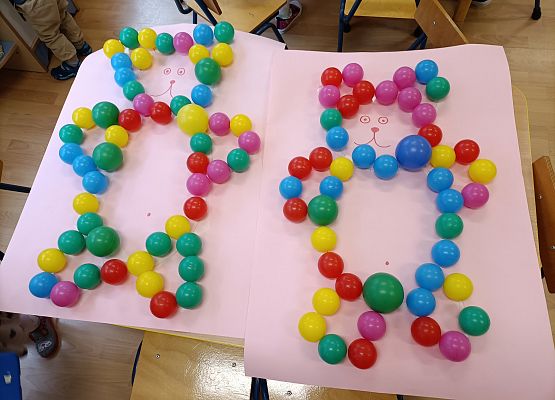 Dziewczynki przyklejają piłki na narysowany kontur misia