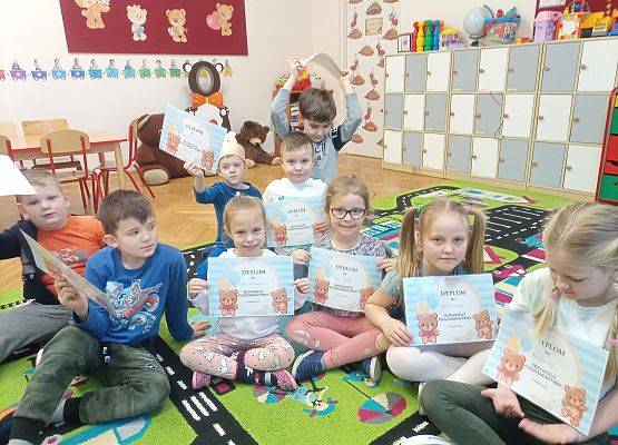 Dzieci siedzą na podłodze i pokazują otrzymane dyplomy