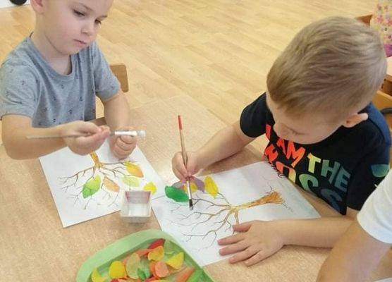 Dwaj chłopcy siedzą przy stoliku i przyklejają kolorowe listki