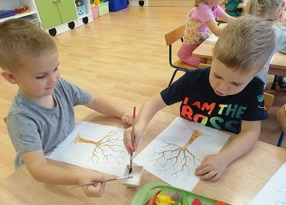 Dwaj chłopcy siedzą przy stoliku i malują na kartce drzewa