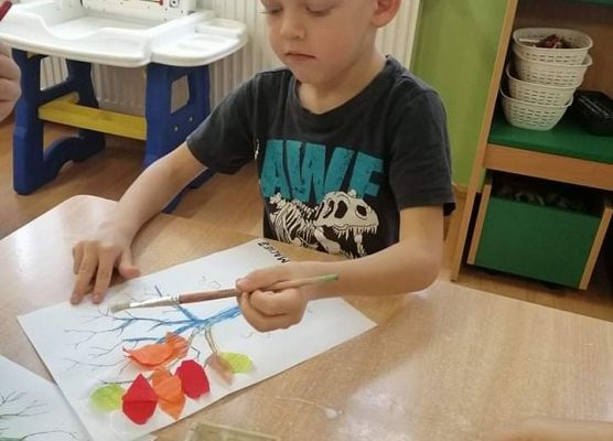 Chłopiec maluje drzewo na kartce papieru