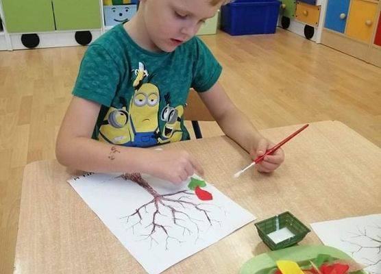 Chłopiec maluje drzewo na kartce papieru