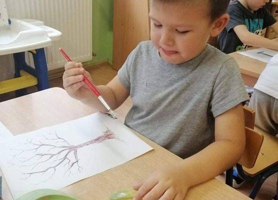 Chłopiec maluje drzewo na kartce papieru