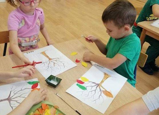 Dzieci malują drzewka jesienne na kartkach papieru
