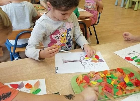 Dziewczynka przykleja papierowe liście do kartki papieru