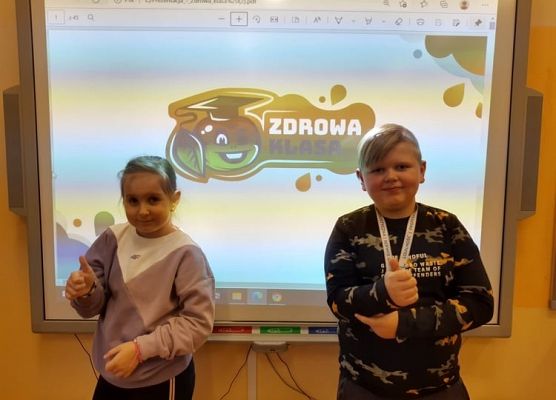 Uczniowie stoją przy tablicy, w tle logo projektu