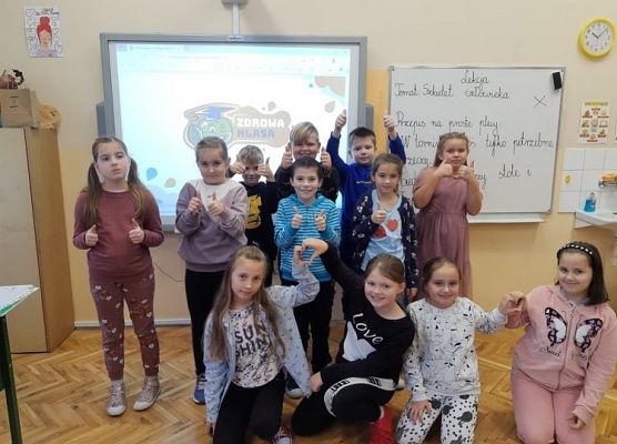 Uczniowie stoją przy tablicy, w tle logo projektu