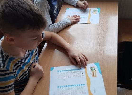 Uczniowie siedzą w ławkach i zapoznają się z ankietą