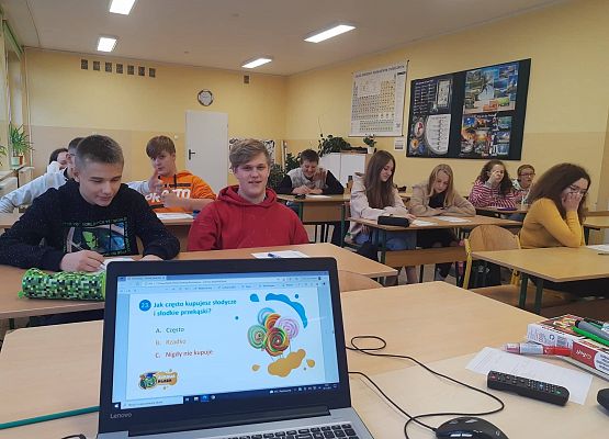 Uczniowie wypełniają ankietę, na stoliku stoi laptop z logiem projektu