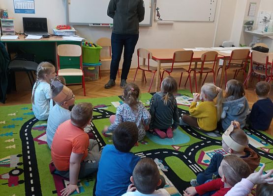 Gość ze Słowińskiego Parku Narodowego stoi i opowiada dzieciom. Dzieci siedzą na dywanie.