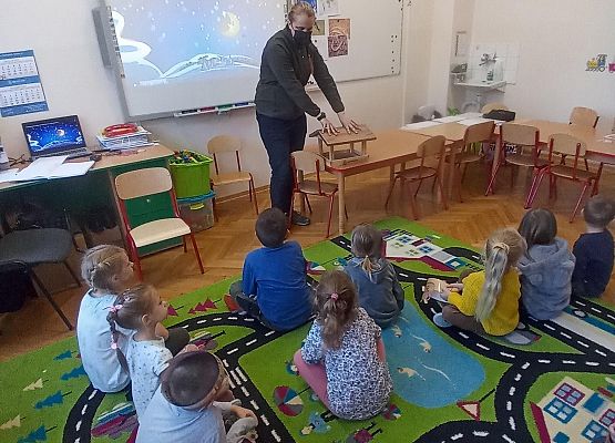 Gość ze Słowińskiego Parku Narodowego stoi i opowiada dzieciom. Dzieci siedzą na dywanie.