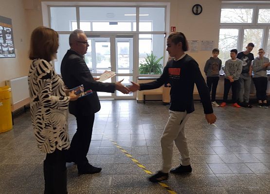 Pan Dyrektor i Pani Wicedyrektor wręczają uczniowi  nagrodę