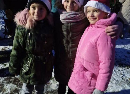 Troje dzieci stoi w czerwonych mikołajkowych czapkach