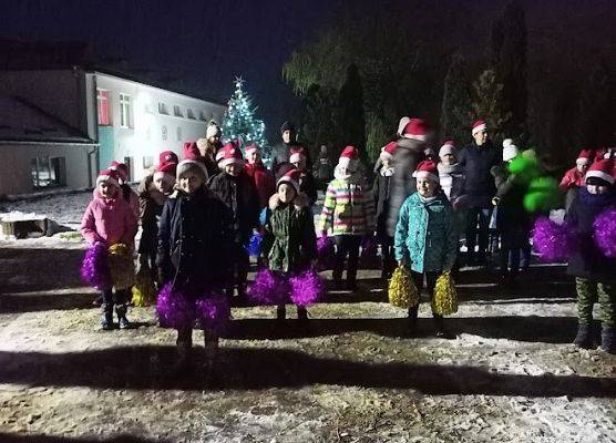 Grupa dzieci z kolorowymi pomponami tańczy na placu