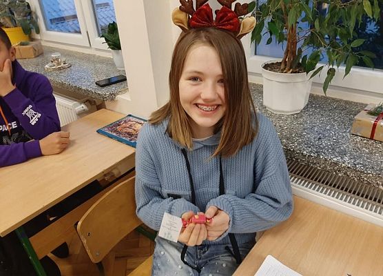 Uczennica siedzi w ławce i trzyma w dłoniach życzenia, które otrzymała od Wolontariusza