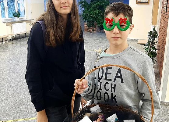 Uczniowie stoją w holu i trzymają koszyk  pełen upominków dla wolontariuszy