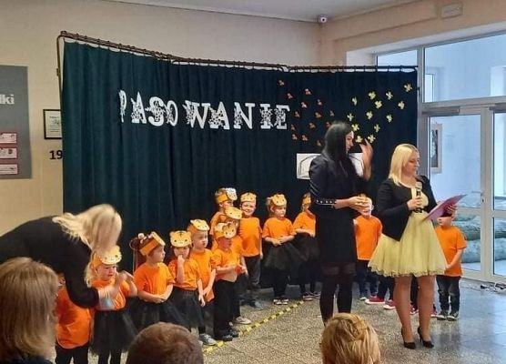 Grupa przedszkolaków w strojach tygrysich stoi na tle dekoracji przed nimi dwie panie nauczycielki