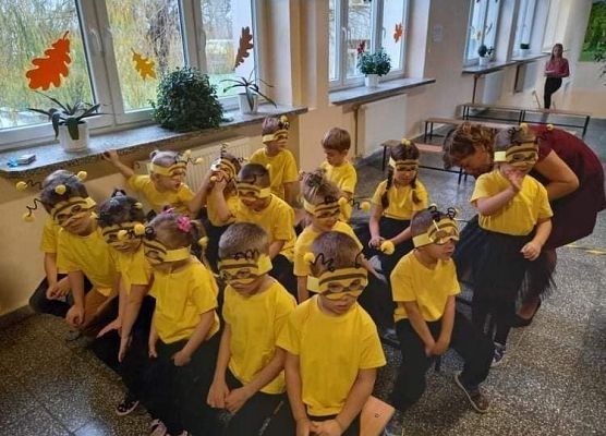 Grupa przedszkolaków przebranych za pszczółki siedzi na ławkach