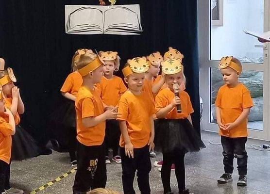 Grupa przedszkolaków przebrana za tygryski stoi na tle zielonej zasłony