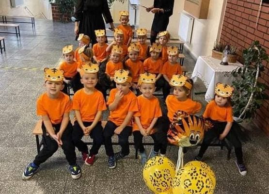 Dzieci przebrane za tygryski siedzą na ławkach za mini stoją dwie panie