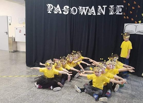 Dzieci przebrane za pszczółki siedzą i trzymają rozłożone ręcce