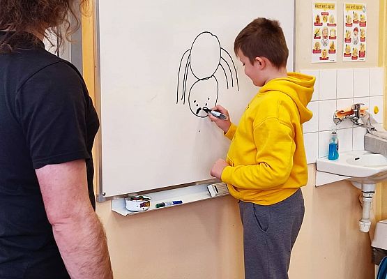 Uczeń rysuje pająka na tablicy.