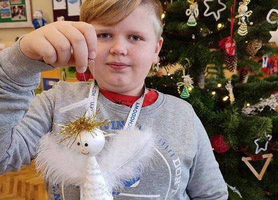 Uczeń stoi przy choince i prezentuje ozdobionego aniołka