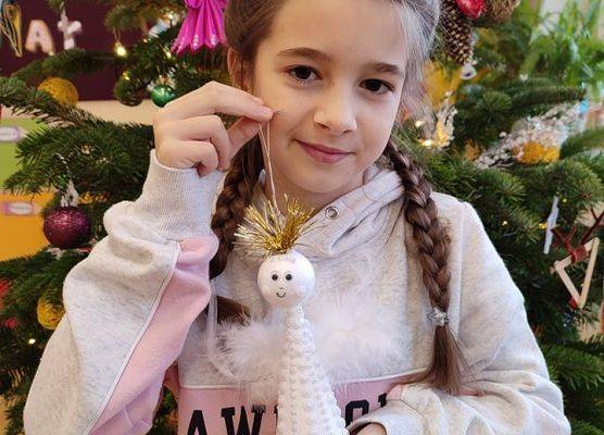 Uczennica stoi przy choince i prezentuje aniołka